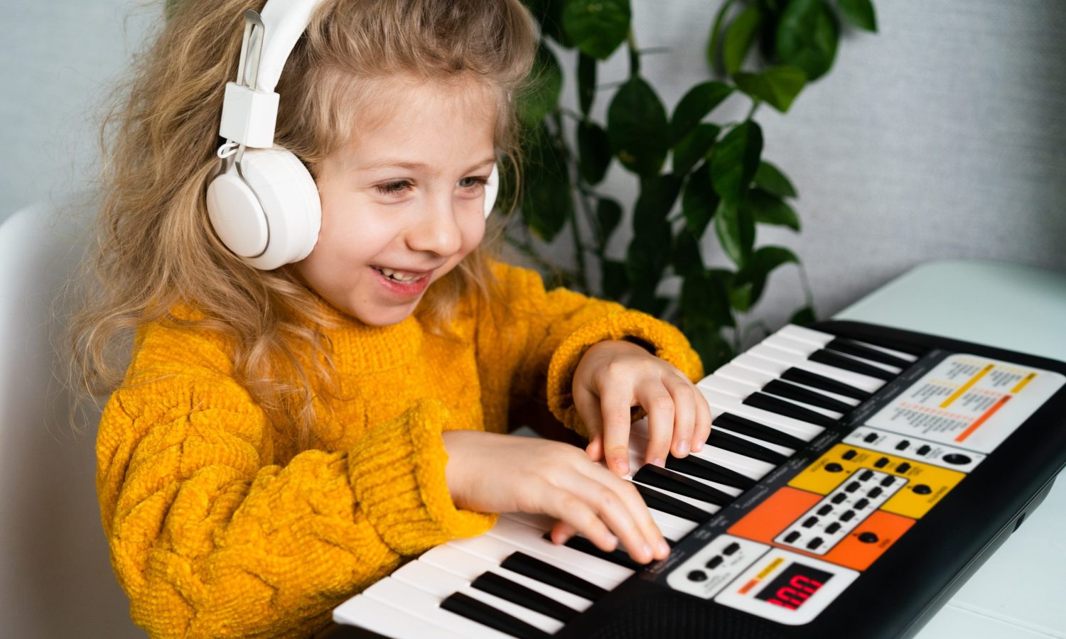 a little blonde girl in headphones smiling and playing the synthesizer, the concept of teaching children music.